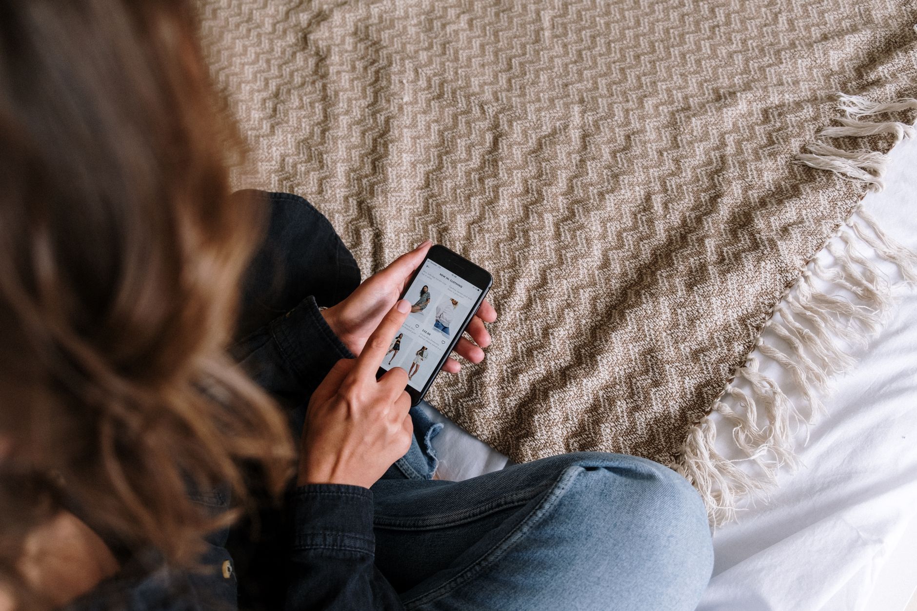 Hands holding a smartphone showing a UK secondhand shopping app with clothing listed for sale